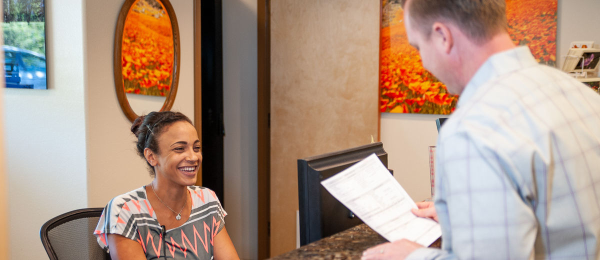 A patient checks in at the Yosemite Dental Care front desk, with framed California poppy photographs on the wall.